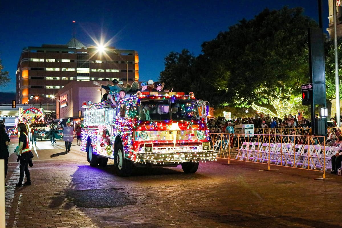 A fire truck decorated with holiday lights in the parade at night.